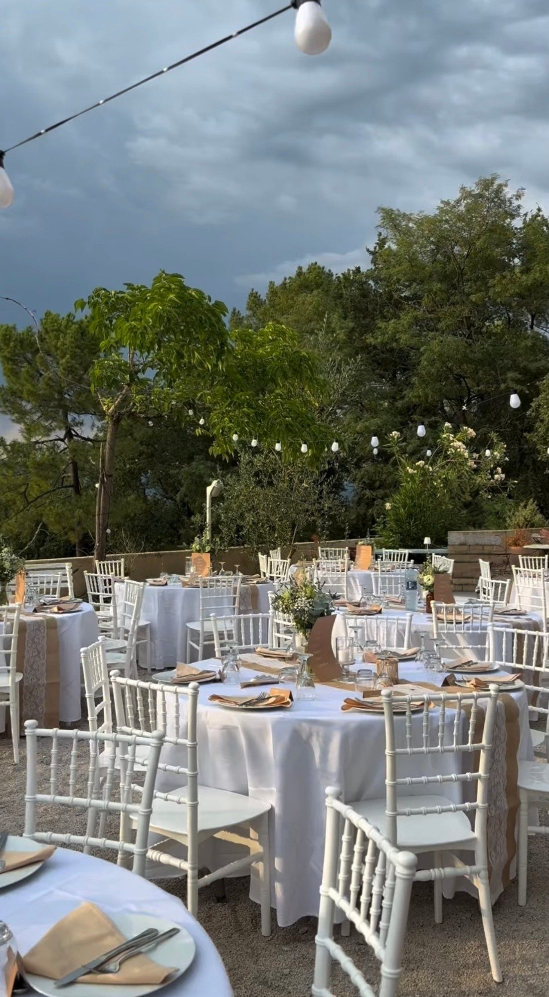 Round tables laid for a wedding dinner beneath festoon lights on the terrace at La Pousterle de Sabran