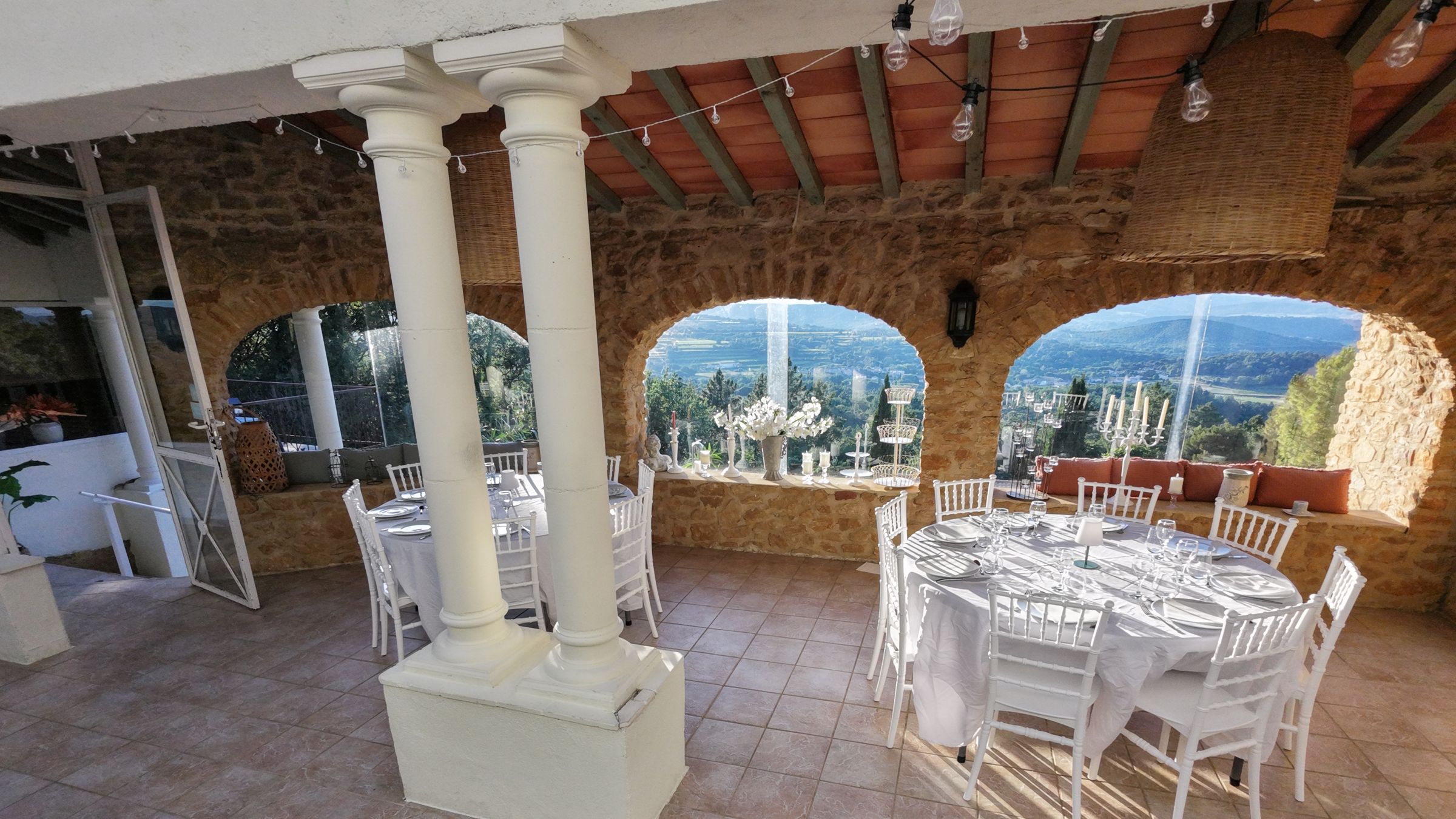 Stone reception room with arches opening onto the valley, tables laid for a wedding at La Pousterle de Sabran