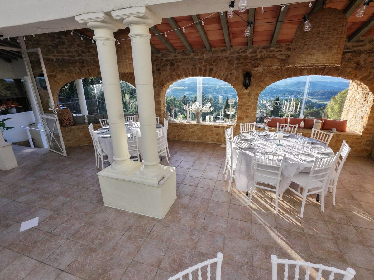 The covered reception space at La Pousterle de Sabran: tables laid between the columns, beneath stone arches open to the valley